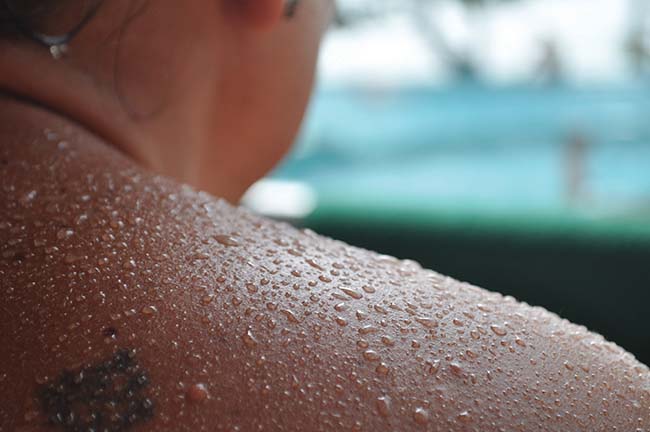 A person’s shoulder and neck are shown and their skin is covered in beads of liquid.